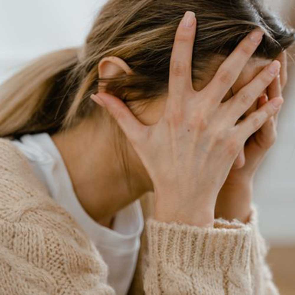 A woman, seated and dressed in blue jeans and a grey sweater, places both her hands on her knees.
